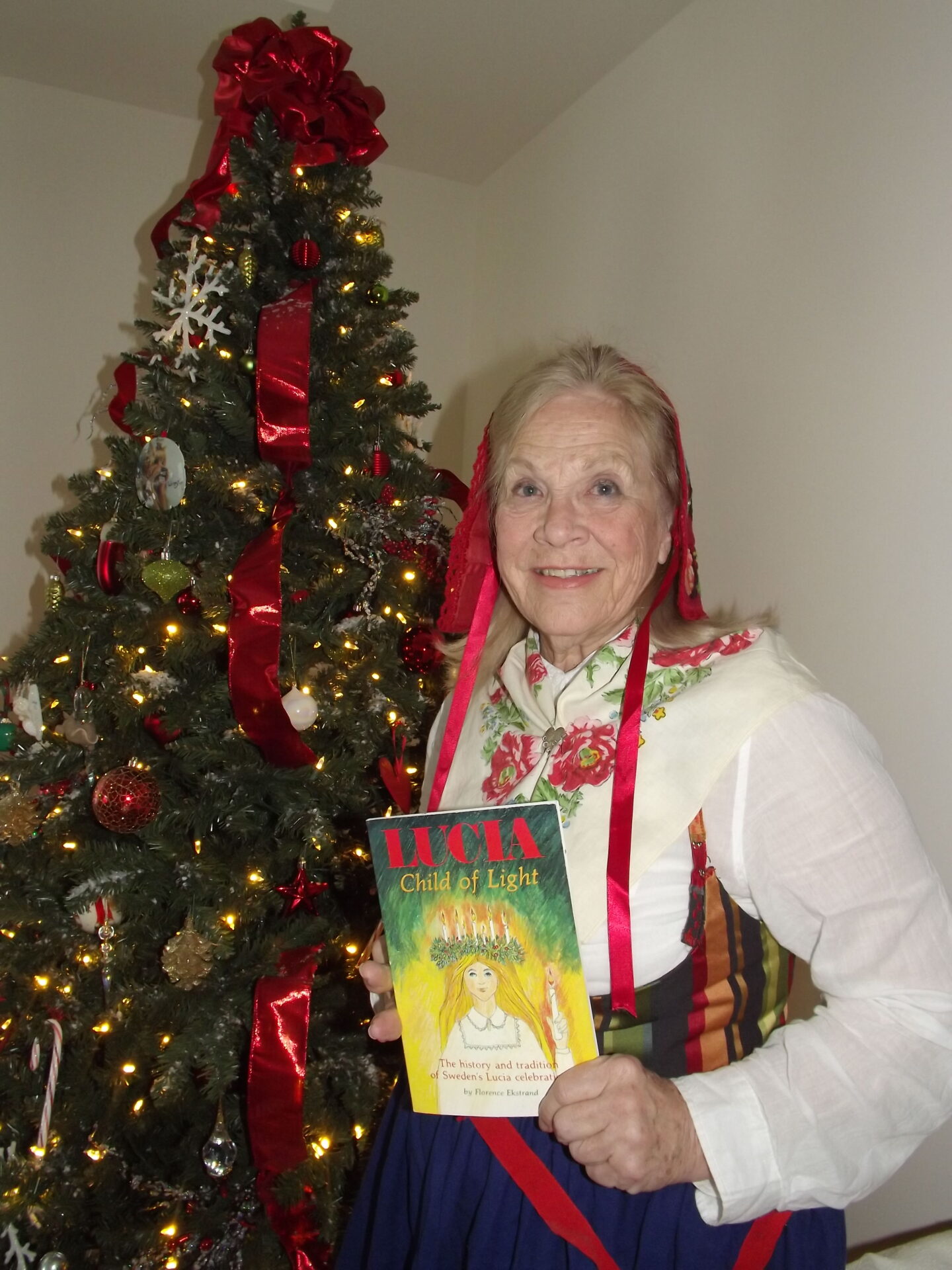 A woman holding a book in front of a christmas tree.